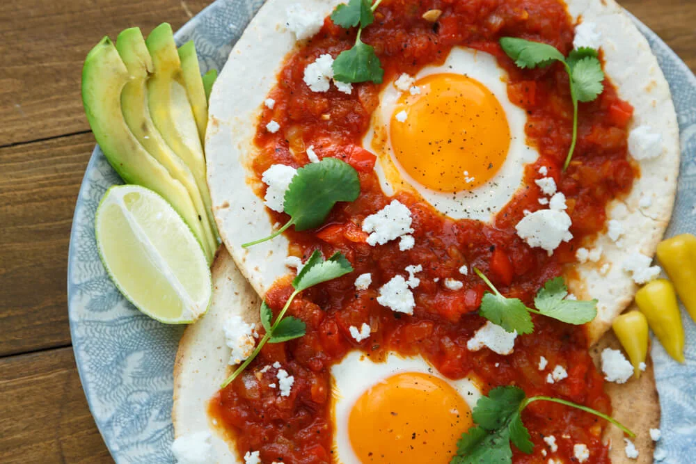 Huevos rancheros with fried eggs, salsa, crumbled cheese, avocado, and lime